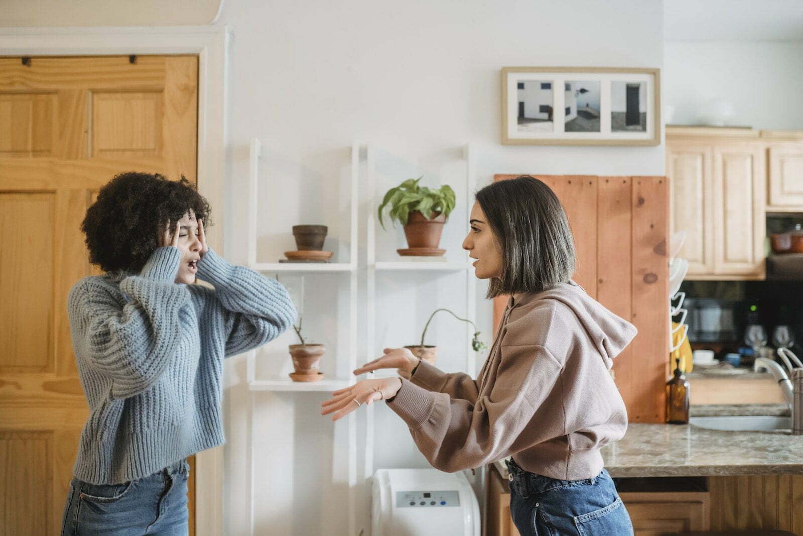 Side view of African American woman with closed eyes quarreling with female wile standing in light room near kitchen at home