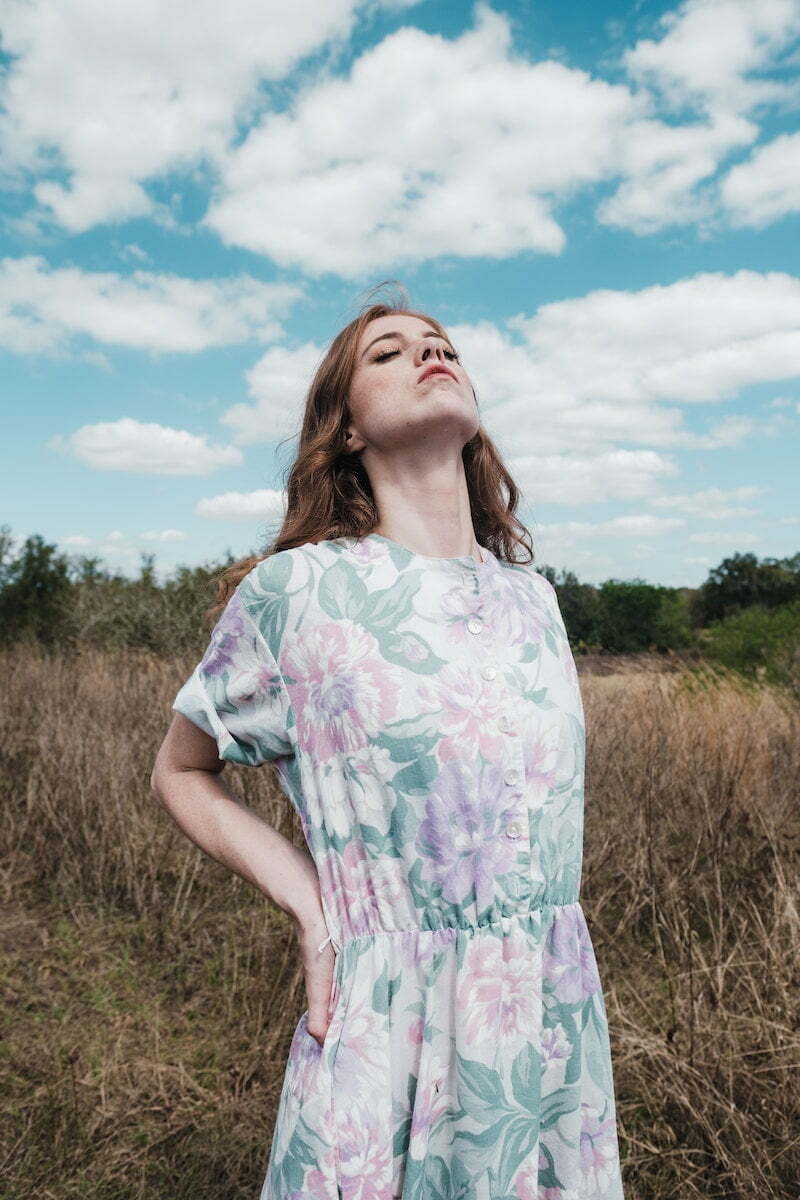 Woman in White and Red Floral Dress Standing on Green Grass Field Under Blue Sky during