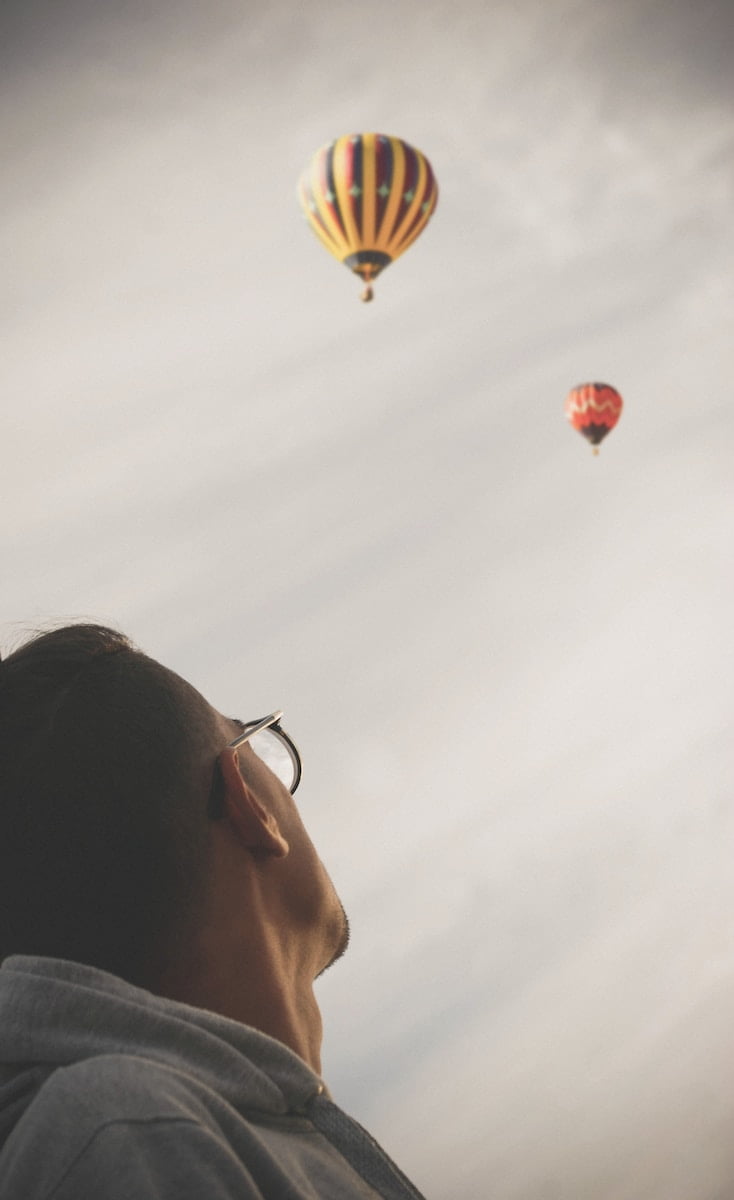 man looking at two hot air balloons in the sky